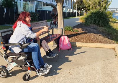 Elisha Matthews in her wheelchair next to a child enjoying time outdoors during Queensland Walks Month