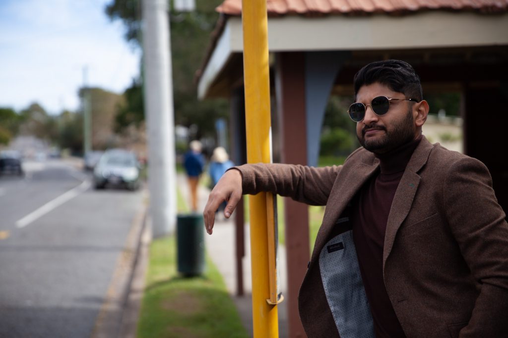 Ritwik Swain stands leaning against a bus sign waiting for the bus