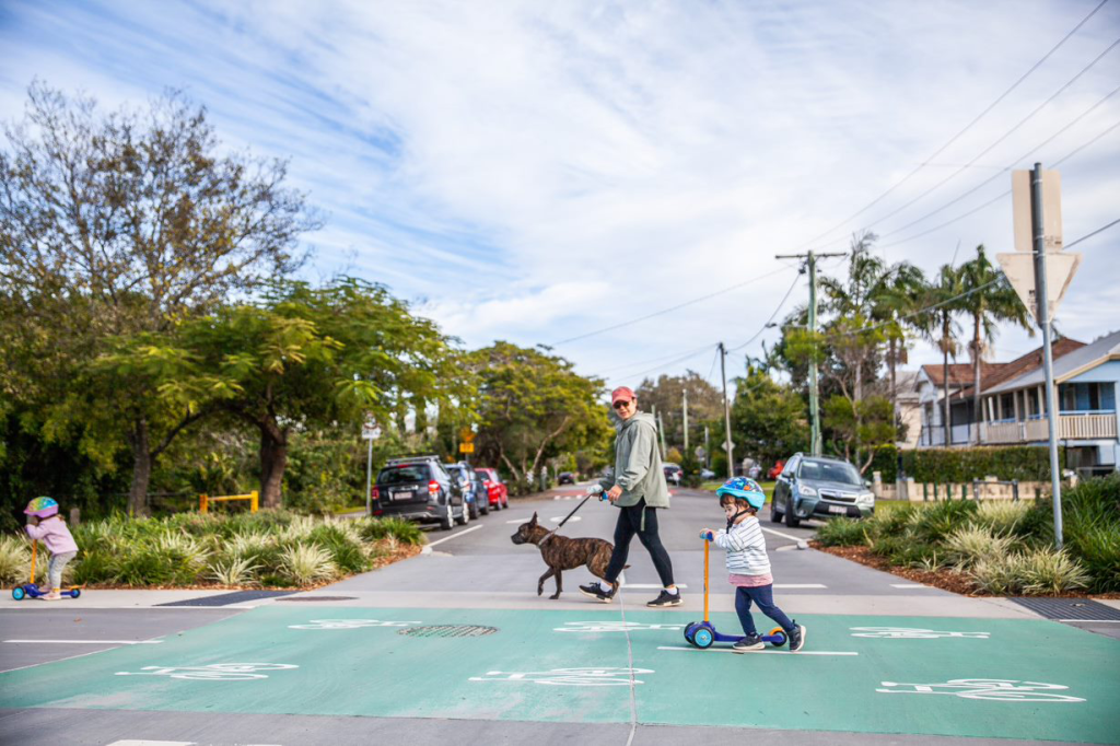 Man walking a dog, young child on scooter on marked raised level crossing.